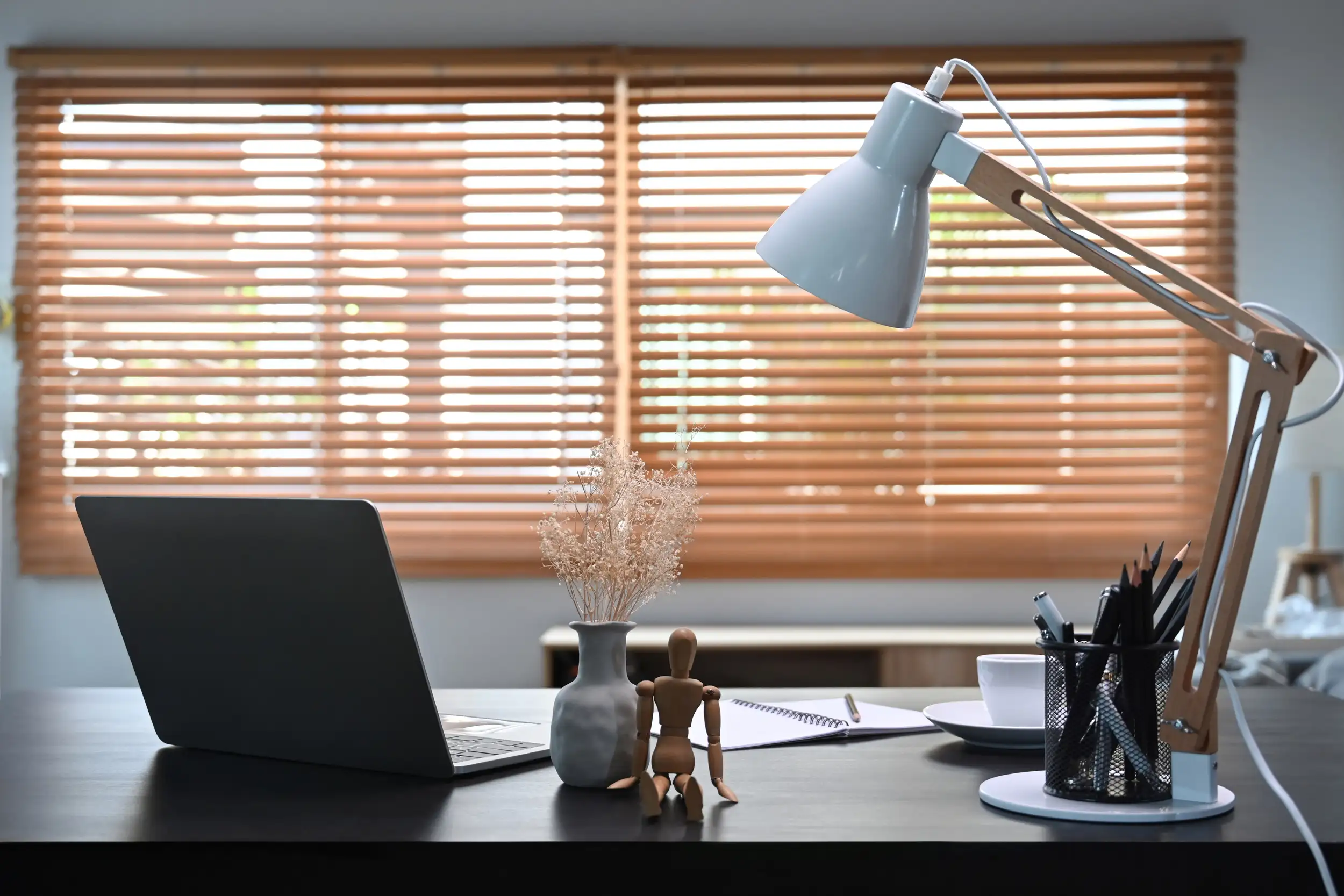 An office desk with window blinds at the back.